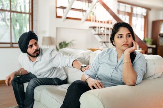 A couple sitting on a couch indoors, appearing upset and in conflict. Emotional tension.